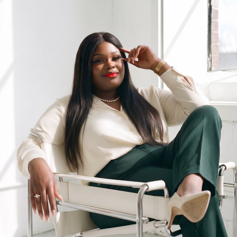 Tiffany Elle seated by a window in a cream blouse